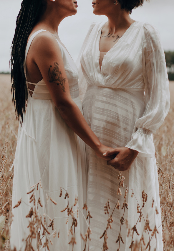 Two Women in Wedding Dresses Holding Hands in Cereal Field